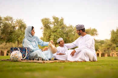 Enjoying drinks, the concept of a happy family, an Omani Gulf Arab family wearing traditional attire sitting in an outdoor park, gestures of happiness and joy, spending the weekend outside.