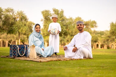Looking at the camera with gestures of happiness and joy, playing and having fun with children in the park, the concept of fitness and physical agility, enjoying engaging in youth activities and sports, an Omani Gulf Arab family wearing traditional attire spending enjoyable time outdoors.