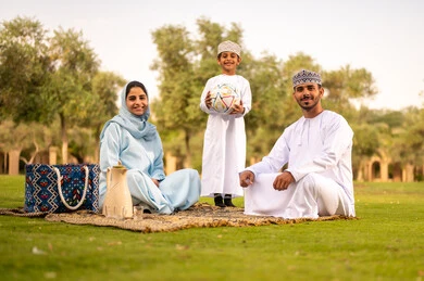 Playing and having fun with children in the park, the concept of fitness and physical agility, enjoying engaging in youth activities and sports, looking at the camera with gestures of happiness and joy, an Omani Gulf Arab family wearing traditional attire spending enjoyable time outdoors.