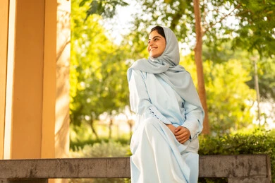 سيده عمانية تقوم بنشاط ترفيهي مسلي، قضاء وقت ممتع في الحديقة العامة، فتاة عربية خليجية سعودية مبتسمة ترتدي الحجاب والعباءة تنظر إلى شيء ما بإيماءات السرور والسعادة، الاستمتاع بالركض في الطبيعة الخضراء في الهواء الطلق