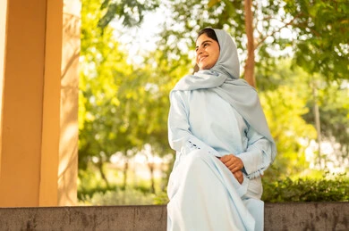 قضاء وقت ممتع في الحديقة العامة، سيده عمانية تقوم بنشاط ترفيهي مسلي، فتاة عربية خليجية سعودية مبتسمة ترتدي الحجاب والعباءة تنظر إلى شيء ما بإيماءات السرور والسعادة، الاستمتاع بالركض في الطبيعة الخضراء في الهواء الطلق