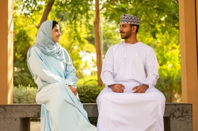 An atmosphere filled with love and affection, strolling in the open air, the concept of successful and happy marital relationships, spending the weekend in one of the parks, an Arab Gulf couple from Oman wearing traditional attire exchanging conversations and chats.