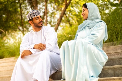 قضاء عطلة نهاية الاسبوع في أحد الحدائق ، مفهوم العلاقات الزوجية الناجحة السعيده،  التنزه في الهواء الطلق ،زوجان عربيان خليجيان عمانيان يرتديان الزي التقليدي يقومان بتبادل الأحاديث والدردشات، اجواء مليئة بالمحبة والود