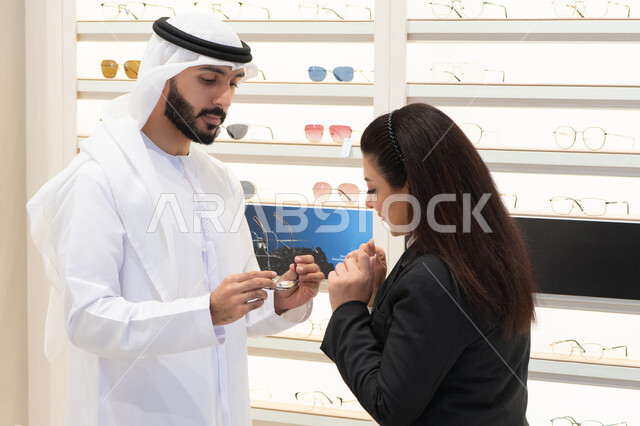 اقتناء النظارات الطبية الجديدة،  شراء الاكسسورات في المولات ، سيده اماراتيه تقوم بمساعده الزبائن في اختيار المقاسات المناسبه لهم، الاهتمام بالمظهر الخارجي، مفهوم ضعف النظر، رجل اماراتي يرتدي الكندوره والغتره البيضاء يقوم باختيار النظارة المناسبة