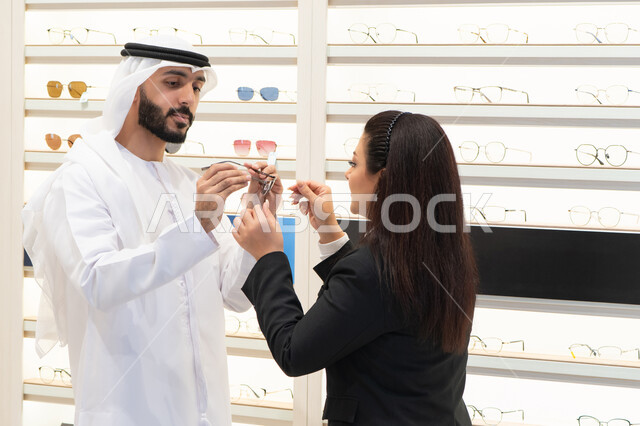 شراء النظارات الطبية، مفهوم ضعف النظر، التسوق والتبضع من المولات ،  رجل اماراتي يرتدي الكندوره والغتره البيضاء يقوم باختيار النظارة المناسبة، سيده اماراتيه تقوم بمساعده الزبائن في اختيار المقاسات المناسبه لهم،الاهتمام بالمظهر الخارجي