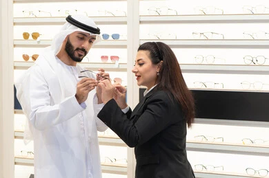 مفهوم ضعف النظر، التسوق والتبضع من المولات ،  رجل اماراتي يرتدي الكندوره والغتره البيضاء يقوم باختيار النظارة المناسبة، ارفف عرض النظارات فى احدي المحلات ، سيده اماراتيه تقوم بمساعده الزبائن في اختيار المقاسات المناسبه لهم،الاهتمام بالمظهر الخارجي