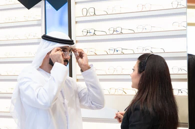 Emirati woman helping customers choose the right sizes for them, the concept of weak eyesight, an Emirati man wearing a white kandura and ghutra choosing the right eyeglasses, taking care of one's appearance, shopping and buying eyeglasses from malls