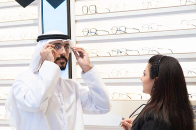 The concept of poor eyesight, an Emirati woman helping customers choose the right sizes for them, an Emirati man wearing a white kandura and ghutra choosing the right eyeglasses, taking care of one's appearance, shopping and buying eyeglasses from malls
