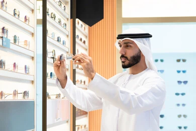 أحدث المنتجات العصرية الحديثة, رجل اماراتي يرتدي الكندوره والغتره البيضاء يقوم بشراء النظارة المناسبة في محل اماراتي،تسوق وشراء  متابعة آخر صيحات الموضة والجمال,الركن الخاص بالنظارات الشمسيه الفخمه ،الاهتمام بالمظهر الخارجي