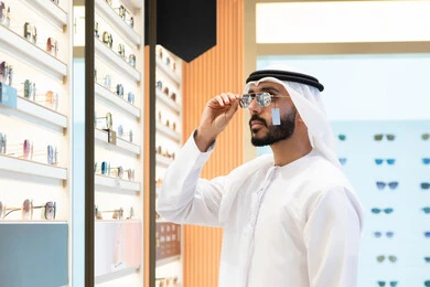 تسوق وشراء أحدث المنتجات العصرية الحديثة, متابعة آخر صيحات الموضة والجمال,الركن الخاص بالنظارات الشمسيه الفخمه ،الاهتمام بالمظهر الخارجي، رجل اماراتي يرتدي الكندوره والغتره البيضاء يقوم بشراء النظارة المناسبة في محل اماراتي