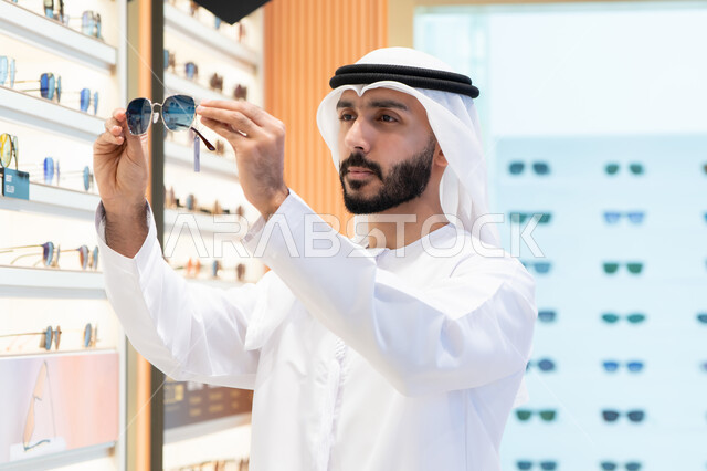 الاهتمام بالمظهر الخارجي، الركن الخاص بالنظارات الشمسيه الفخمه ،رجل اماراتي يرتدي الكندوره والغتره البيضاء يقوم بشراء النظارة المناسبة في محل اماراتي ،  التسوق والتبضع من المولات