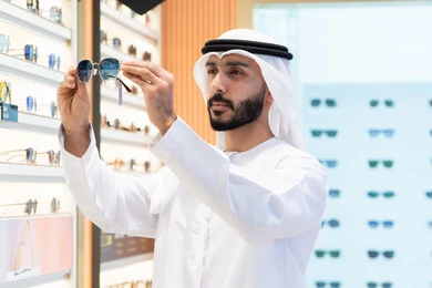 الاهتمام بالمظهر الخارجي، الركن الخاص بالنظارات الشمسيه الفخمه ،رجل اماراتي يرتدي الكندوره والغتره البيضاء يقوم بشراء النظارة المناسبة في محل اماراتي ،  التسوق والتبضع من المولات