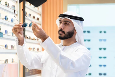 The luxury sunglasses corner, taking care of one's appearance, an Emirati man wearing a white kandura and ghutra buying the right pair of glasses in an Emirati store, shopping in malls.