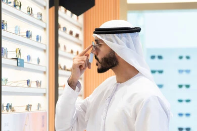 انواع وماركات النظارات العالميه، ايماءات الثقه في النفس ،الفحص قبل الشراء، متعة التسويق والتبضع باختيار نظارة شمسيه مناسبة، رجل عربي خليجي اماراتي يرتدي الكندوره يقوم بقياس نظاره سوداء