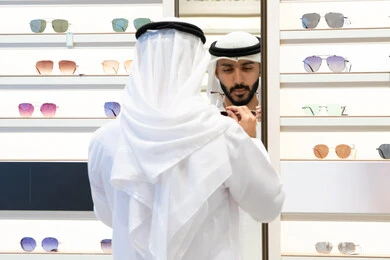 التسوق فى احدي المولات الاماراتيه ،الحيرة في الاختيار ، فحص النظارات الطبيه قبل الشراء، متعة التسويق والشراء، صورة مقربة لرجل عربي خليجي اماراتي يرتدي الكندره يقوم باختيار نظاره مناسبه