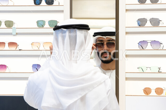 متعة التسويق والشراء ، فحص النظارات قبل الشراء، صورة مقربة لرجل عربي خليجي اماراتي يرتدي الكندره يقوم باختيار نظاره طبيه، الحيرة في الاختيار