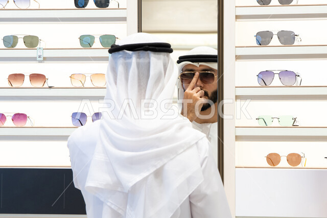 فحص النظارات قبل الشراء، متعة التسويق والشراء ، صورة مقربة لرجل عربي خليجي اماراتي يرتدي الكندره يقوم باختيار نظاره طبيه، الحيرة في الاختيار