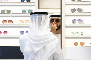 Checking glasses before buying, the joy of shopping and buying, a close-up of an Emirati Gulf Arab man wearing a kandara choosing glasses, the confusion of choosing