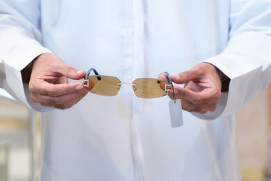 صورة مقربة ليد رجل عربي خليجي اماراتي يرتدي الكندره يقوم باختيار نظاره طبيه، فحص النظارات قبل الشراء، الحيره فى اختيار نظاره مناسبه ، متعة التسويق والشراء