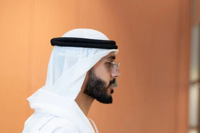 قياس النظارات الشمسيه السوداء قبل الشراء، متعة التسويق والشراء، صورة مقربة لرجل عربي خليجي اماراتي يرتدي الكندوره يقوم بقياس نظاره شمسيه، تعابير الحيرة في الاختيار ، الاهتمام بالمنظر الخارجي