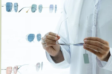 Buying sunglasses from malls, shopping experience and choosing eyeglasses, close-up of the hand of a young Emirati Gulf Arab man wearing a kandura choosing suitable sunglasses in an optical shop, taking care of one's appearance