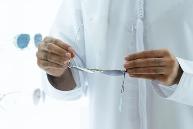 اقتناء النظارات من احدى المولات الاماراتيه ، صورة مقربه ليد شاب عربي اماراتي خليجي يرتدي الكندوره يقوم باختيار النظارة الشمسيه المناسبة في محل نظارات ، الاهتمام بالمظهر الخارجي، التسوق وشراء من المولات