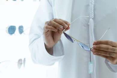 صورة مقربه ليد شاب عربي اماراتي خليجي يرتدي الكندوره يقوم باختيار النظارة الشمسيه المناسبة في محل نظارات ،تجربة التسوق و اختيار النظارات الطبية ، الاهتمام بالمظهر الخارجي، التسوق وشراء النظارات الشمسيه من المولات،