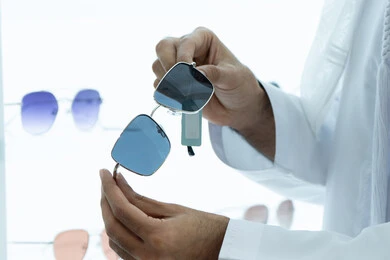 Shopping and buying sunglasses from malls, a close-up photo of the hand of a young Emirati Gulf man wearing a kandura choosing the right sunglasses in an optical shop, the concept of elegance and interest in one's outward appearance