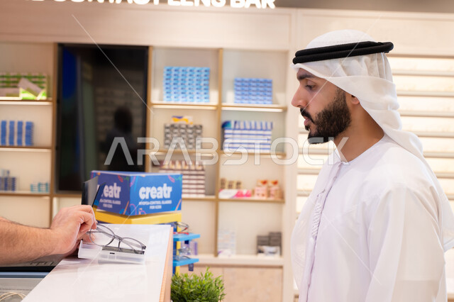 شراء النظارات الخاصة بضعف النظر، تحسين الرؤية ومحاولة تعديل البصر، شاب عربي خليجي اماراتي يرتدي الكندوره والغتره البيضاء يقوم بشراء النظارة الطبيه المناسبة في محل نظارات , الاهتمام بالمظهر الخارجي، التسوق وشراء النظارات الطبيه