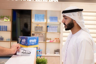 Buying glasses for weak eyesight, improving vision and trying to correct vision, a young Emirati Gulf Arab man wearing a white kandura and ghutra buying suitable eyeglasses in an optics store, taking care of one's appearance, shopping and buying eyeglasses