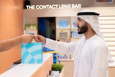 تطبيقات التسوق والشراء الالكتروني عبر الهاتف، تسوق وشراء أحدث منتجات النظارات العصرية الحديثة, رجل عربي خليجي اماراتي يحمل كيس ورقي ملون، اقتناء وشراء هدايا من احدي المولات الاماراتيه، إتمام عملية الدفع باستخدام الهاتف المحمول