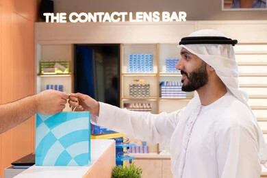 تسوق وشراء أحدث منتجات النظارات العصرية الحديثة, رجل عربي خليجي اماراتي يحمل كيس ورقي ملون، اقتناء وشراء هدايا من احدي المولات الاماراتيه، تطبيقات التسوق والشراء الالكتروني عبر الهاتف، إتمام عملية الدفع باستخدام الهاتف المحمول