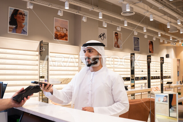 Mobile shopping and purchasing applications, completing the payment process using a mobile phone, purchasing gifts from one of the Emirati malls, an Arab Gulf Emirati man making electronic payments.