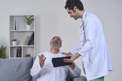 رفع اليدين للاعلى بإيماءات الدعاء وشكر الله، متابعة السجل الطبي الالكتروني, ممرض يرتدي المعطف يقوم بوصف الحالة المرضية باستخدام جهاز التابليت، تقديم أفضل الخدمات الطبية المنزلية، بورتريه لرجل كبير السن عربي خليجي اماراتي يرتدي الكندورة ويجلس على الكنبه، خلفية بيضاء