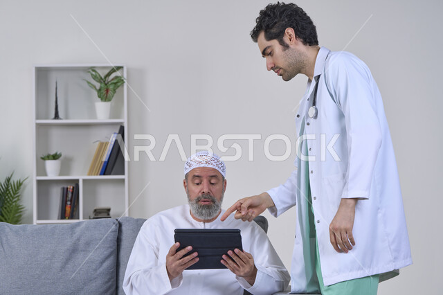 تقديم أفضل الخدمات الطبية المنزلية لمرضى كبار السن، متابعة السجل الطبي الالكتروني الخاص بالمريض, بورتريه لممرض يرتدي اليونيفورم والمعطف يقوم بوصف الحالة المرضية باستخدام جهاز التابليت، مريض مسن عربي خليجي اماراتي يرتدي الكندورة ويجلس على الكنبه، خلفية بيضاء