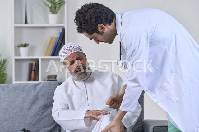 شركات التمرض المنزلي، الحاجة إلى العلاج الفيزيائي، آلام المفاصل والعظام والأعصاب، تقديم أفضل الخدمات الطبية المنزلية للمرضى كبار السن، بورتريه لممرض يرتدي المعطف يقوم بفحص رجل مسن عربي خليجي اماراتي يرتدي الكندورة ويجلس على الكنبه، خلفية بيضاء