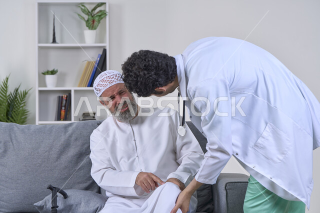 Home nursing companies, need for physical therapy, joint, bone and nerve pain, providing the best home medical services for elderly patients, portrait of a nurse wearing a coat examining an elderly Arab Gulf Emirati man wearing a kandura and sitting on a sofa, white background
