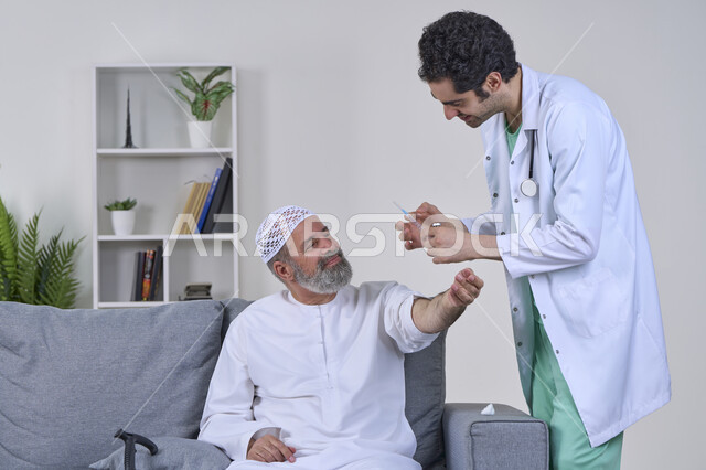 الاستعداد لأخذ الحقنة المسكنة للألم، مفهوم العمل في شركات التمريض المنزلي، تقديم أفضل الخدمات الطبية المنزلية للمرضى كبار السن، بورتريه لممرض يرتدي اللباس الطبي يقوم بإعطاء ابرة لرجل كبير بالسن عربي خليجي اماراتي يرتدي الكندورة ويجلس على كنبه، خلفية بيضاء