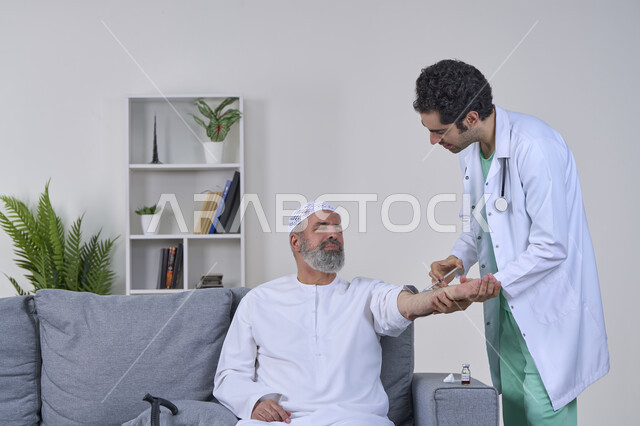 أخذ الحقنة المسكنة للوجع، تعابير الألم الشديد، تقديم أفضل الخدمات الطبية المنزلية للمرضى كبار السن، العمل في القطاع الصحي، بورتريه لممرض اسعافات اولية يرتدي اللباس الطبي يقوم بإعطاء ابرة لرجل كبير بالسن عربي خليجي اماراتي يرتدي الكندورة ويجلس على كنبه، خلفية بيضاء