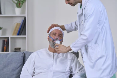 Treating chronic asthma, inhaling medications to treat sleep apnea, maintaining a regular airway using a ventilator, providing home health care, close-up portrait of a nurse in a medical coat applying an oxygen mask to an Arab Gulf Emirati patient, white background