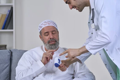 Health awareness and avoiding the spread of infection, following prevention and safety measures against the Corona virus, a doctor holding a digital infrared thermometer, close-up portrait of a nurse examining an elderly Arab Gulf Emirati patient wearing a kandura and hat, working in the medical sector, white background