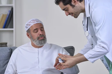 Attention and regular follow-up of home checkups, doctor wearing coat holding digital infrared pulse oximeter, close-up portrait of nurse checking blood oxygen level of elderly Arab Gulf Emirati patient wearing kandura and hat, working in medical sector, white background