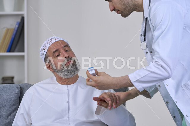 جهاز قياس نسبة أكسجة الدم، المتابعة الدورية للفحوصات المنزلية، طبيب يرتدي المعطف يحمل مقياس الاكسجين ونبضات القلب الرقمي بالأشعة تحت الحمراء، بورتريه مقرب لممرض يقوم بفحص مريض مسن عربي خليجي اماراتي يرتدي الكندورة والقبعة، العمل في القطاع الطبي، خلفية بيضاء