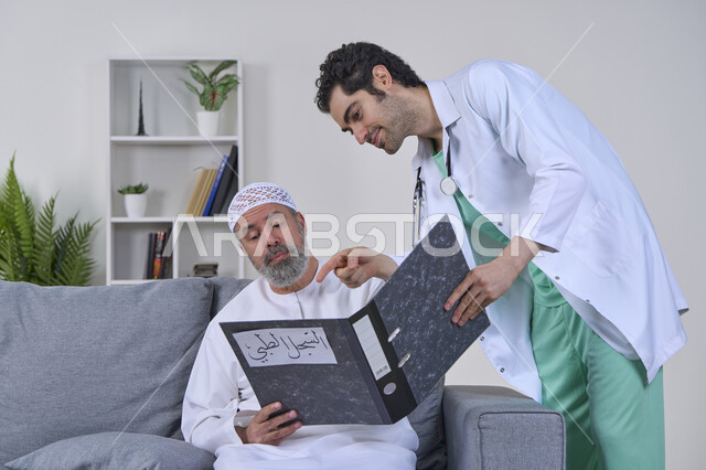Following up on patients' medical records, working in home nursing companies, portrait of a nurse wearing a uniform and a medical coat describing the medical condition of an elderly Arab Gulf Emirati patient wearing a kandura and sitting on a couch, providing the best home medical services to elderly patients, white background