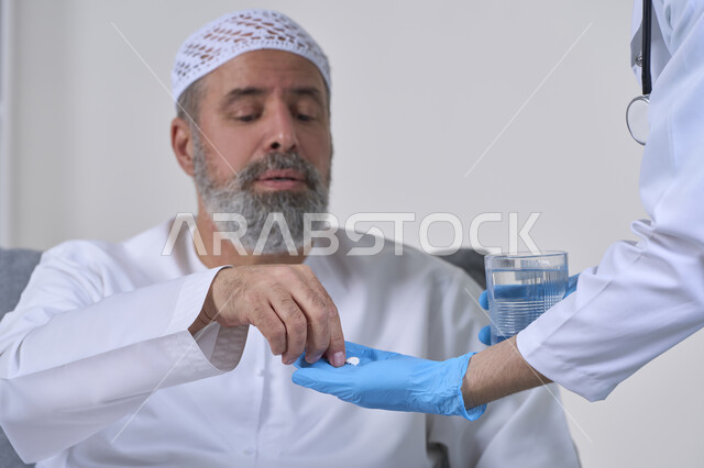 Health care and adherence to the correct times for taking medication, use of prescription medication, working in the medical sector and home nursing companies, close-up portrait of a nurse wearing a medical coat giving medication pills to an elderly Arab Gulf Emirati patient wearing a kandura, white background