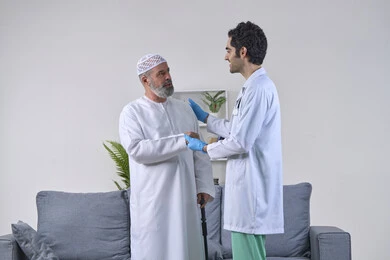 شكر وتقدير الطبيب لجهوده ورعايته الطبية، تقديم أفضل الخدمات الطبية لمرضى كبار السن، العمل في المجال الصحي، بورتريه لرجل عربي خليجي اماراتي مسن يرتدي الكندورة والقبعة ويصافح الممرض بايماءات الامتنان، صورة الجسم بالكامل، خلفية بيضاء