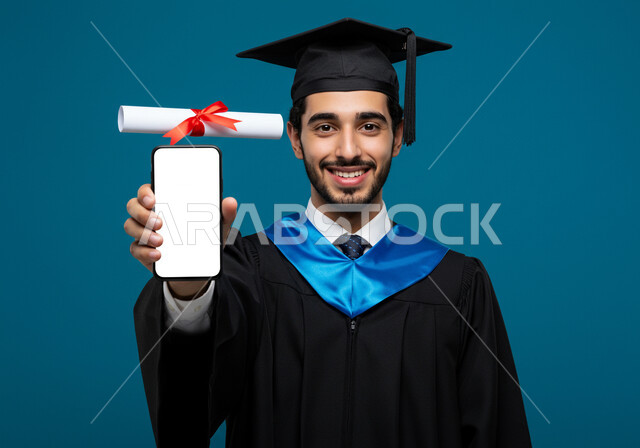 عرض شاشة بيضاء فارغة على الهاتف المحمول، الشعور بالفخر والثقة بالنفس، مفهوم الاجتهاد والتفوق، الاحتفال بإنهاء الدراسة الجامعية، تعابير السرور بالنجاح، بورتريه مقرب لطالب عربي خليجي سعودي يرتدي عباءه وقبعة التخرج يحمل الشهادة بإيماءات الرضا والسرور، خلفية زرقاء