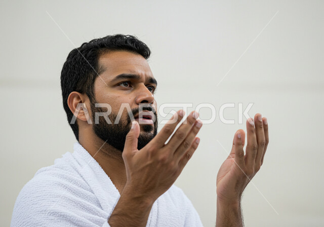 مفهوم أركان الإسلام وأداء الفرائض الدينية، رفع اليدين والدعاء بخشوع وتضرع، بورتريه مقرب لحاج خليجي عربي سعودي يرتدي ثياب الإحرام يقوم بتأدية مناسك الحج والعمرة، العبادة والتقرب إلى الله، خلفية بيضاء