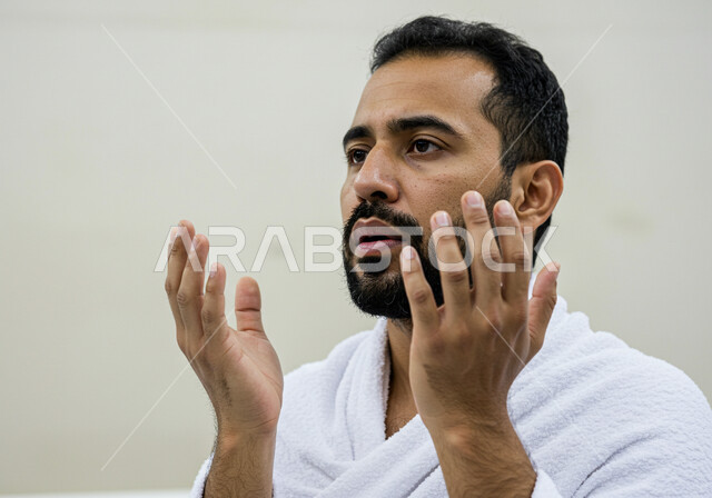 مفهوم أركان الإسلام وأداء الفرائض الدينية، رفع اليدين والدعاء بخشوع وتضرع، بورتريه مقرب لحاج خليجي عربي سعودي يرتدي ثياب الإحرام يقوم بتأدية مناسك الحج والعمرة، العبادة والتقرب إلى الله، خلفية بيضاء