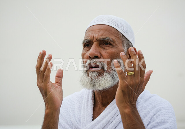مفهوم أركان الإسلام وأداء الفرائض الدينية، رفع اليدين والدعاء بخشوع وتضرع، بورتريه مقرب لحاج خليجي عربي سعودي يرتدي ثياب الإحرام يقوم بتأدية مناسك الحج والعمرة، العبادة والتقرب إلى الله، خلفية بيضاء